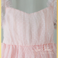 White swiss dot pattern on light pink tulle. Dress has short puffy sleeves and is made to be worn at knee length. 