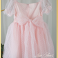 back of dress with a big bow. dress is a swiss dot pattern in light pink with puff short sleeves and knee length style. 